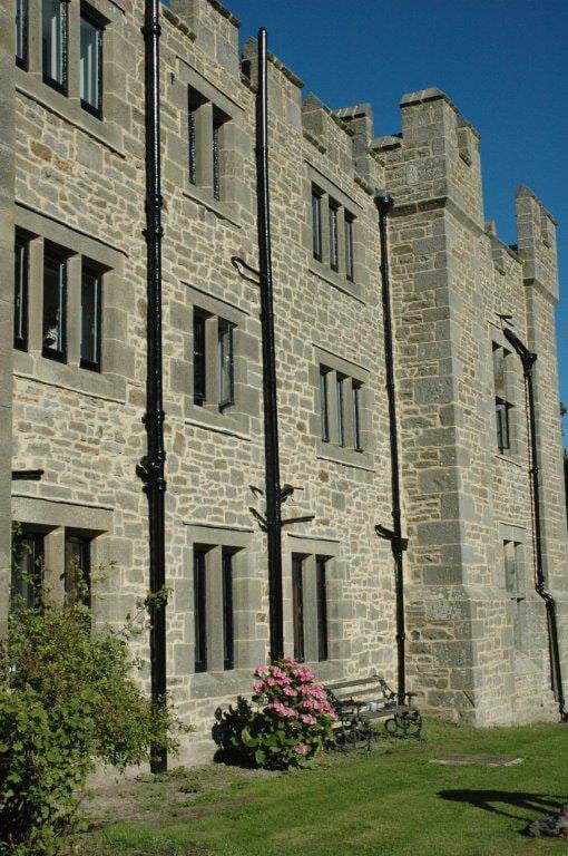 Large stone building with a bench and flowers in front on a clear day